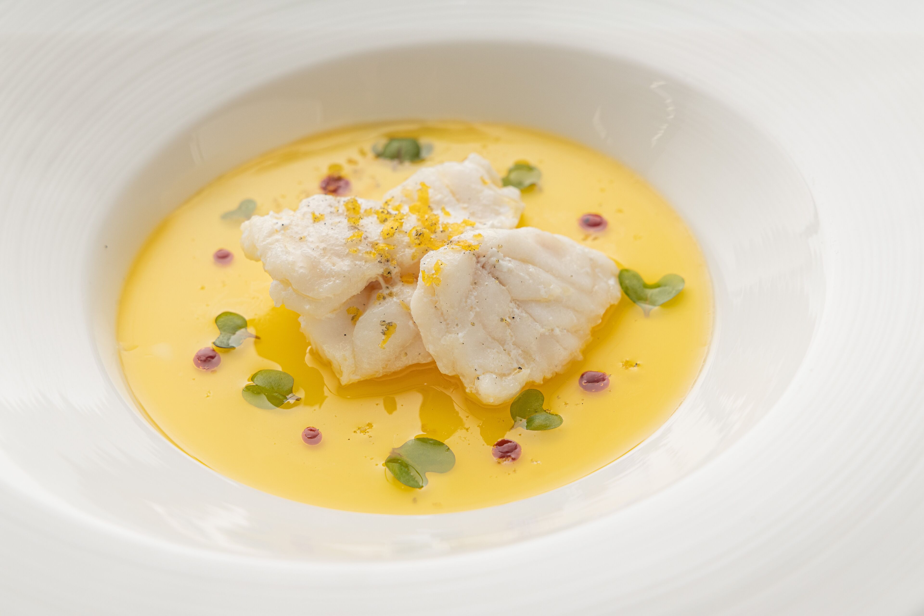 Een witte schaal met gele saus, vis en garnering.