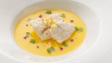 Een witte schaal met gele saus, vis en garnering.