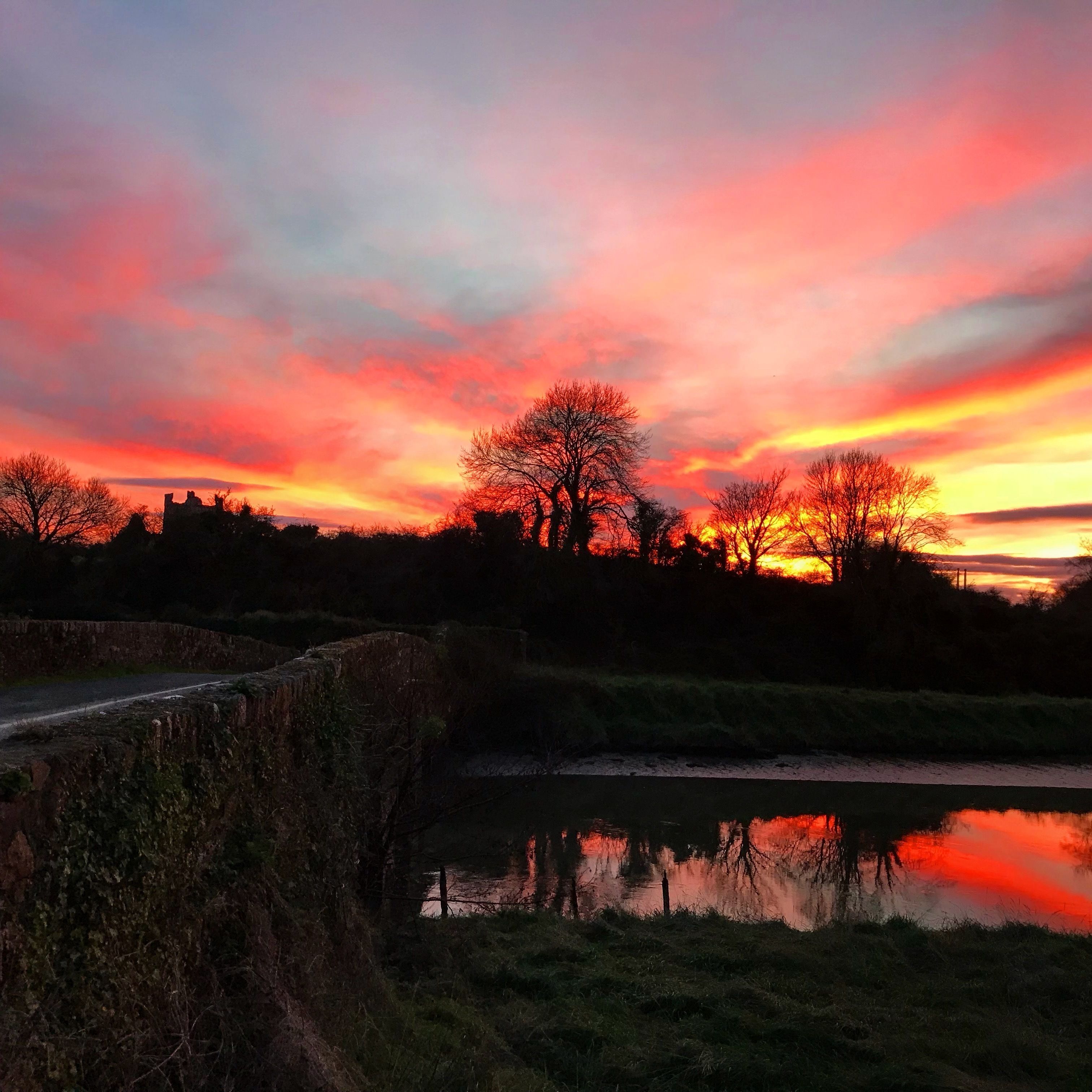 Un atardecer sobre un río con un puente de piedra y árboles silueteados contra el cielo.