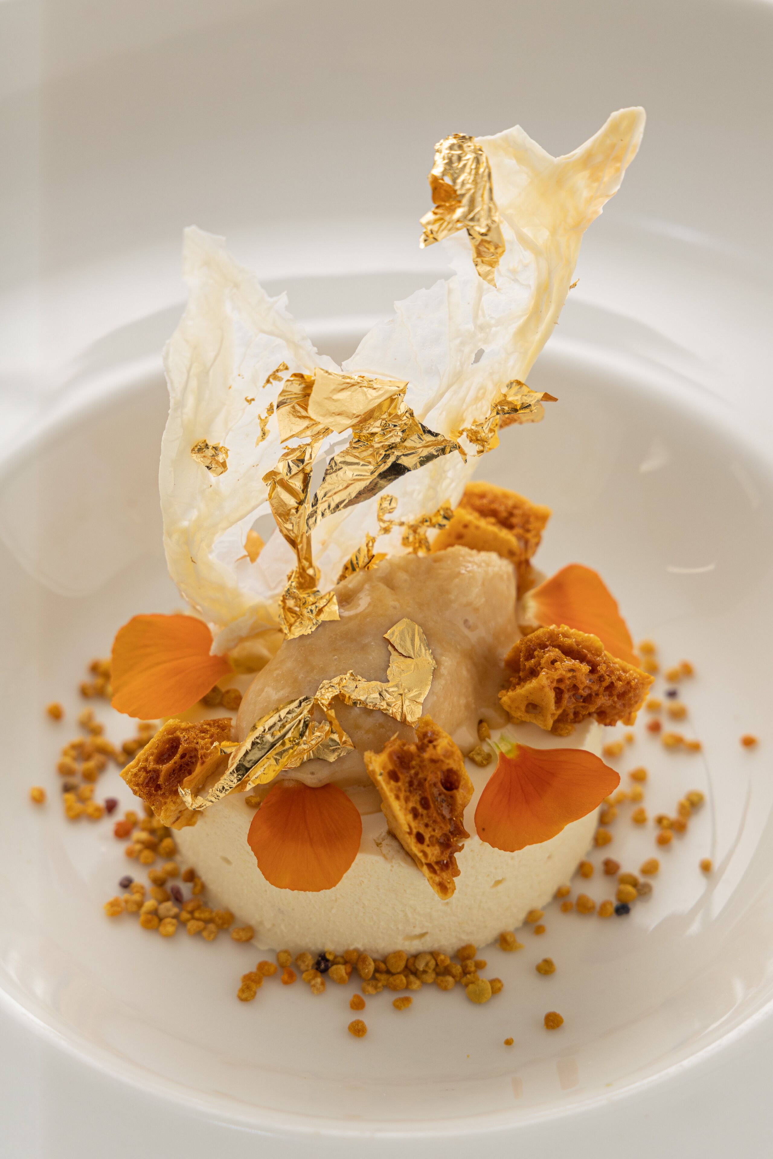 A dessert with a spherical base, golden flakes, and orange petals on a white plate.