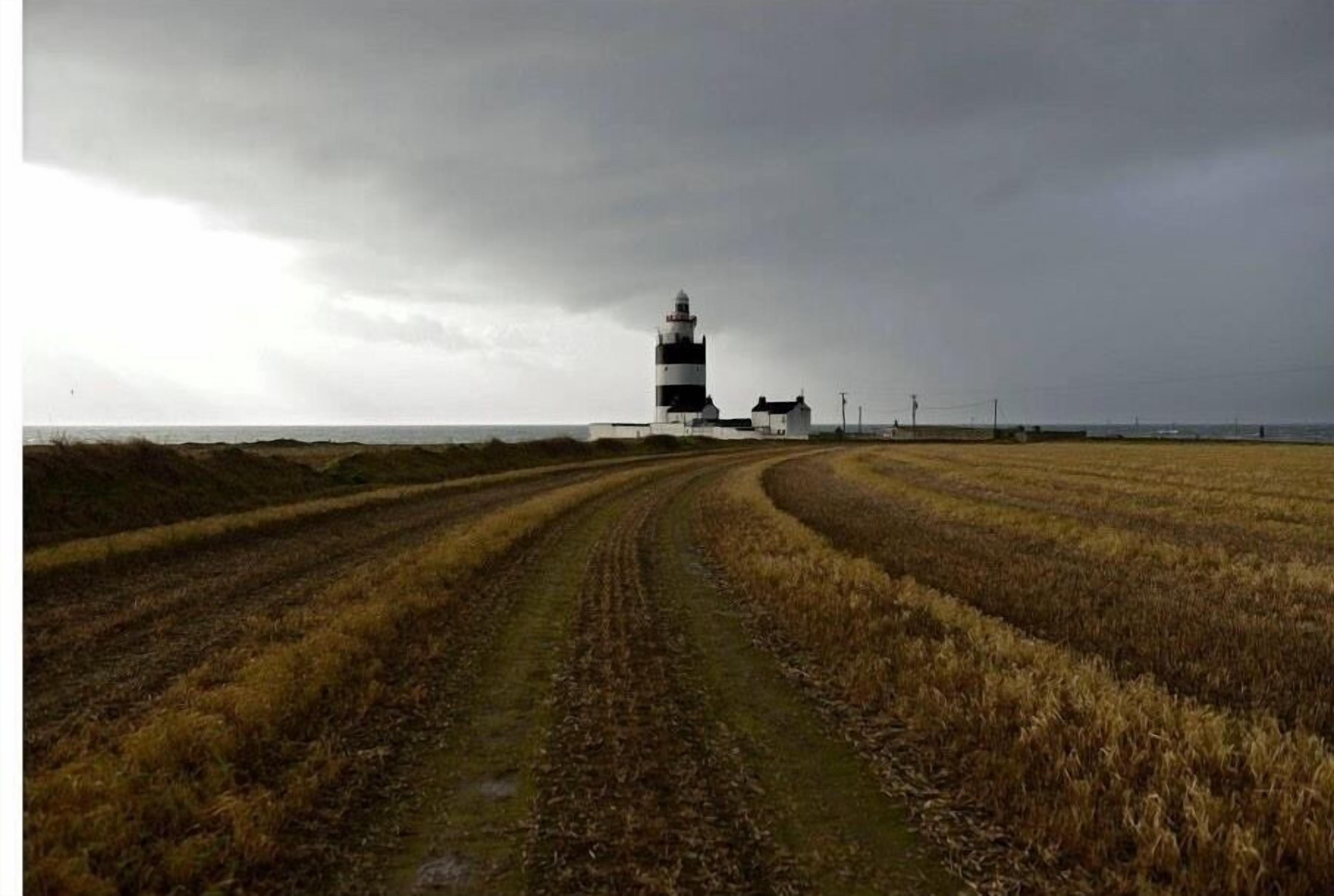Um farol em um campo gramado com uma trilha de terra que leva até ele.