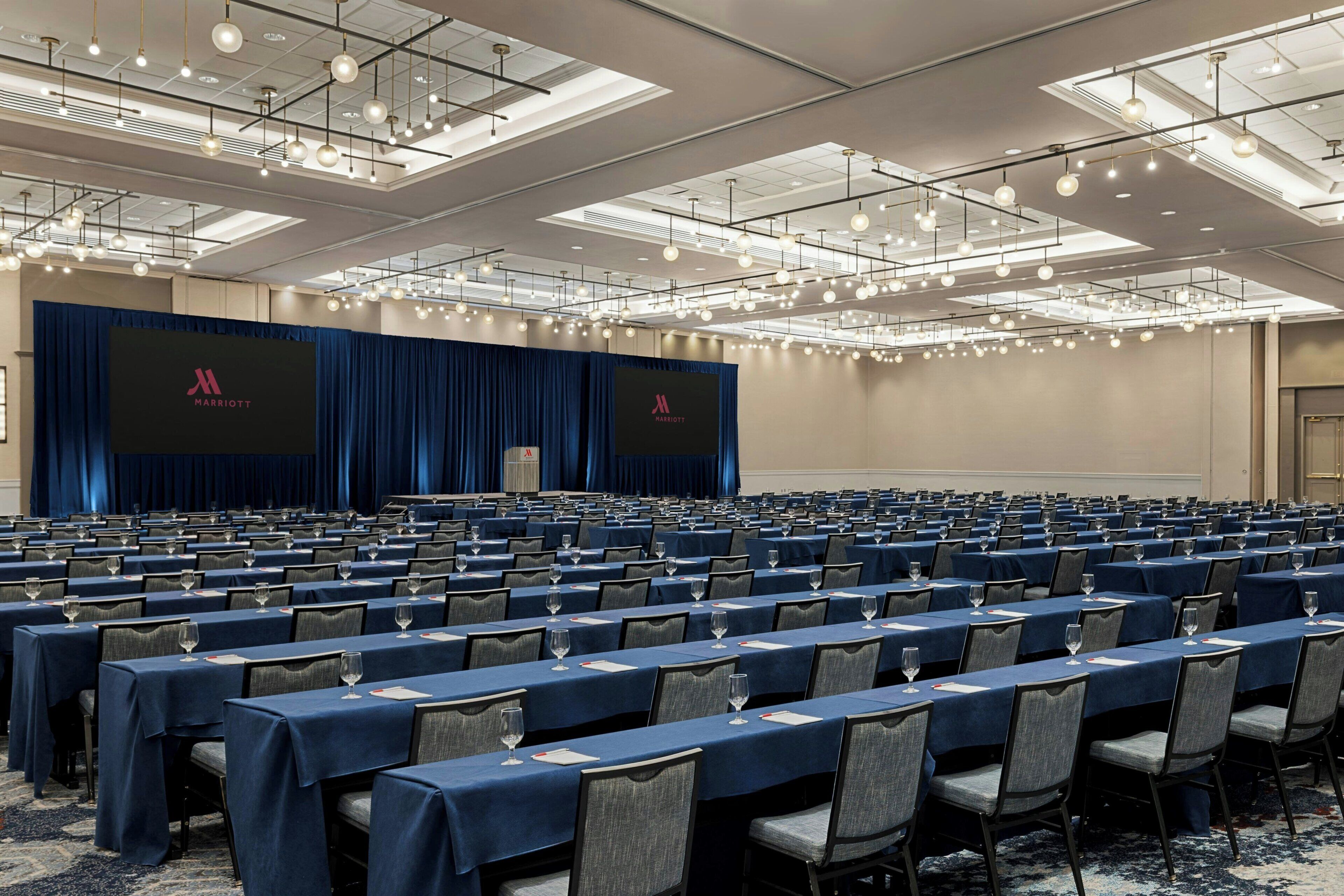 A conference room with rows of tables, chairs, and a stage with a backdrop.