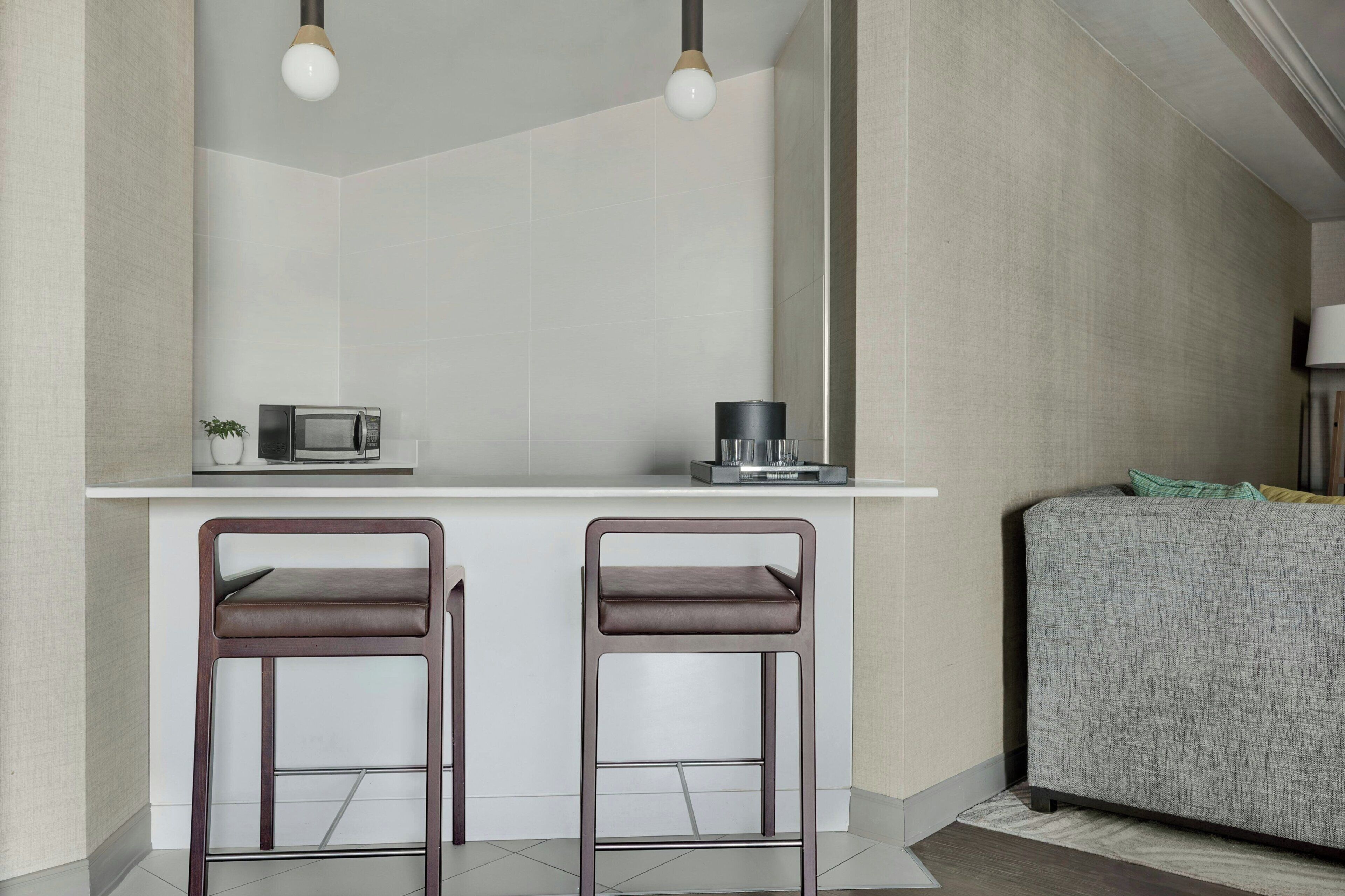 A modern kitchen with a white countertop, two bar stools, a microwave, and a coffee maker.
