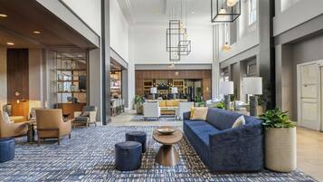 A spacious lobby with a blue patterned carpet, seating area with sofas and chairs, a bar in the background, and pendant lighting.