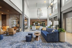 A spacious lobby with a blue patterned carpet, seating area with sofas and chairs, a bar in the background, and pendant lighting. - Mystic Marriott Hotel and Spa (Groton)