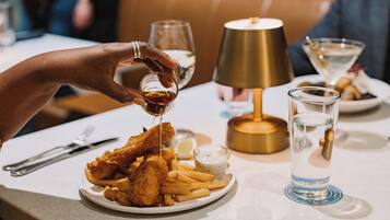 Un plato de pescado con papas fritas, un vaso de agua y una lámpara sobre una mesa.