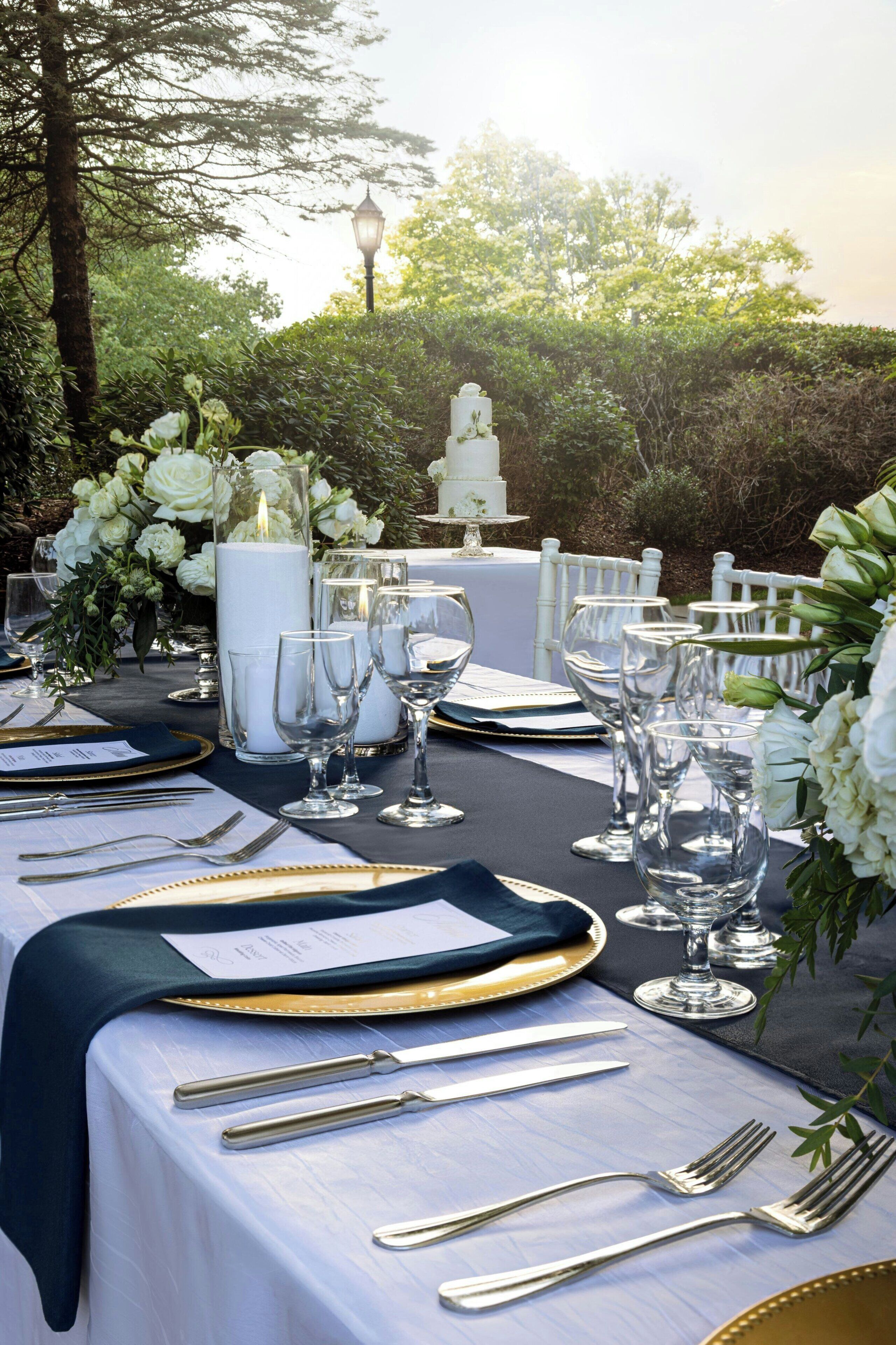 Un espace de restauration en plein air avec une table dressée pour un repas formel, entouré de verdure et agrémenté d’une structure décorative en arrière-plan.