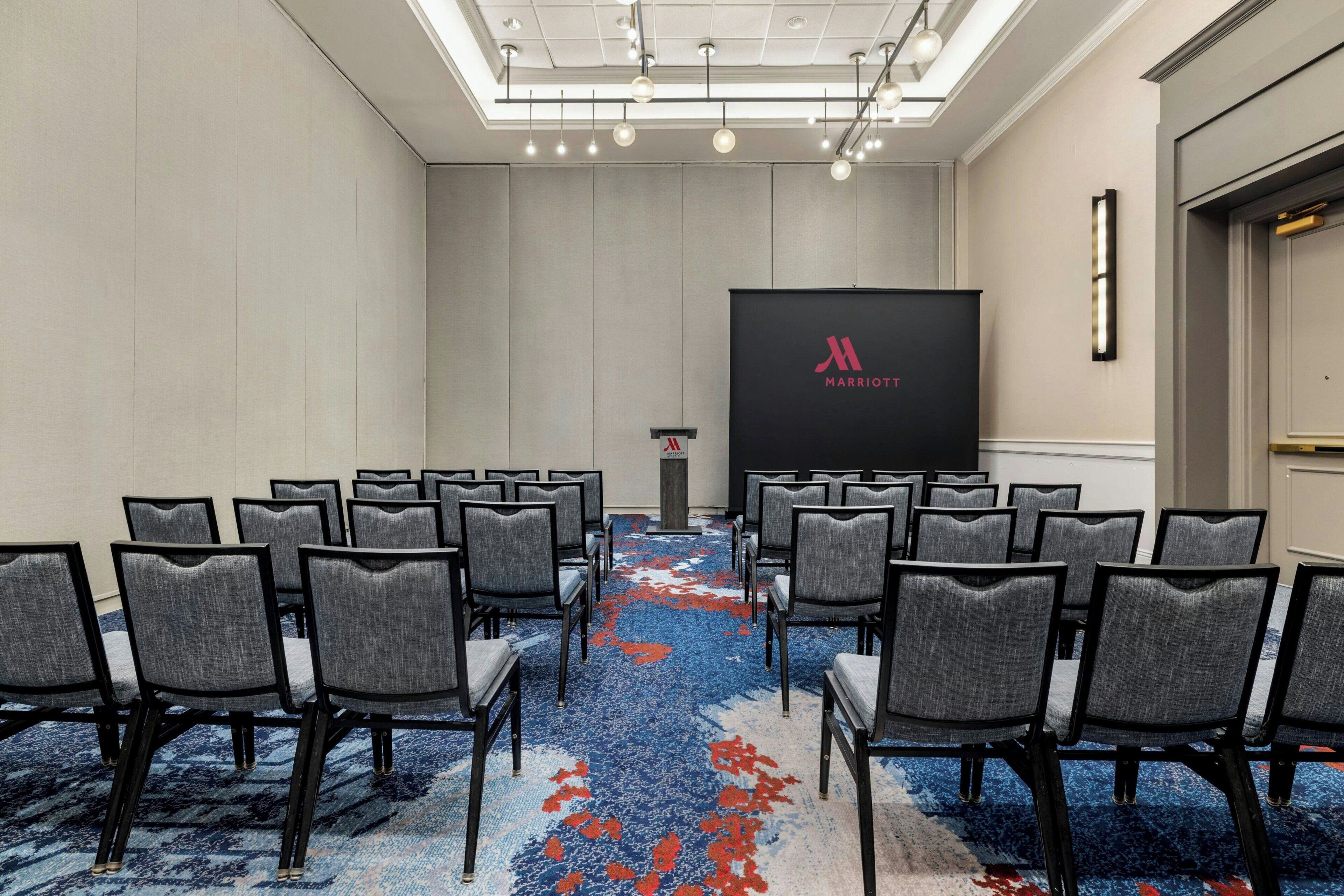 A conference room with rows of chairs, a podium, and a large screen displaying the Marriott logo.