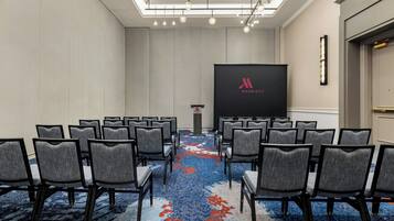 A conference room with rows of chairs, a podium, and a large screen displaying the Marriott logo.