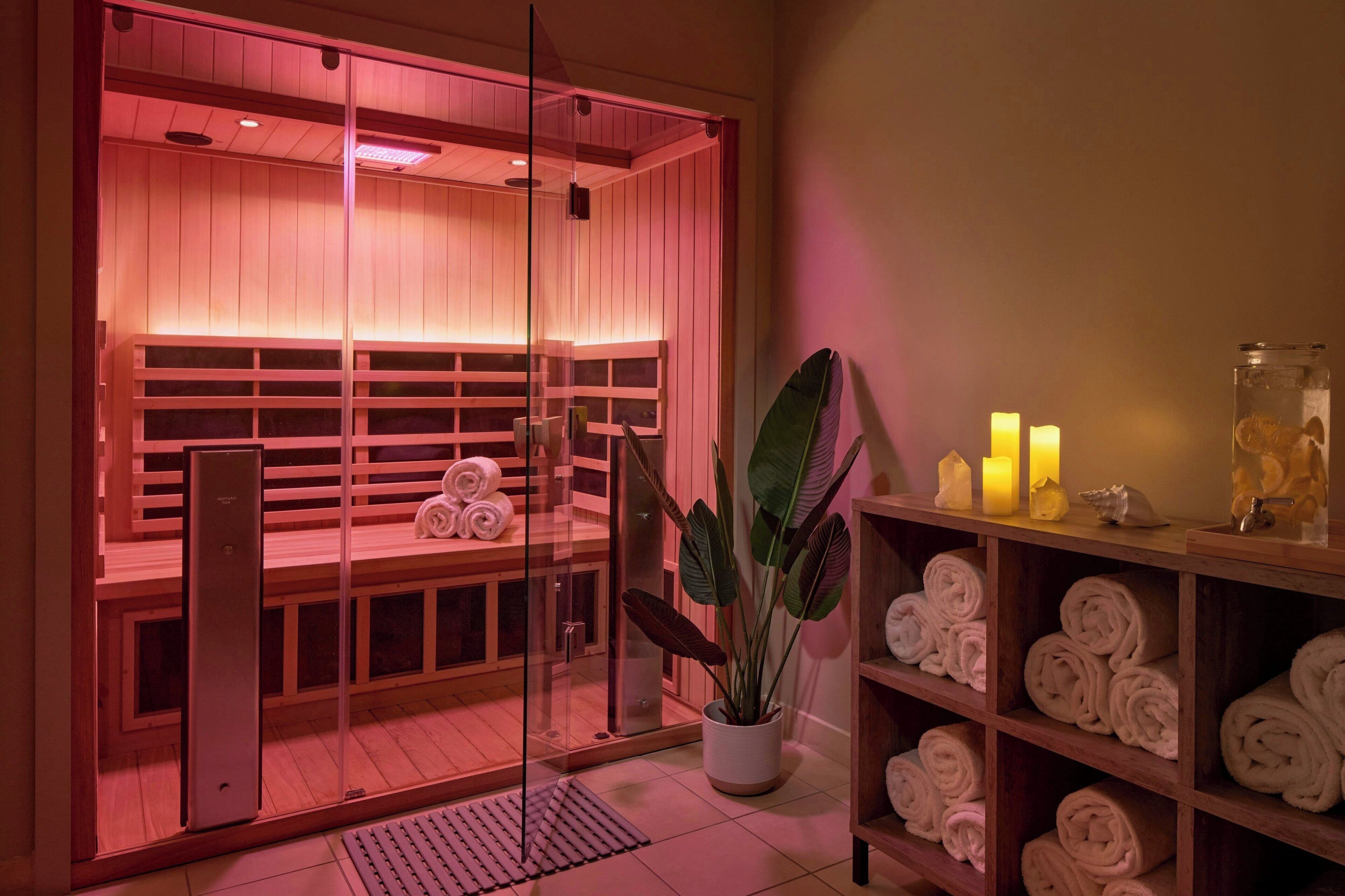 A sauna room with wooden benches, a glass door, and a shelf with towels and candles.