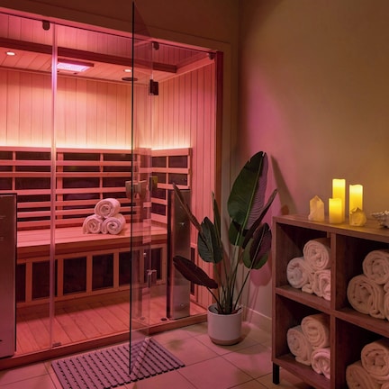 A sauna room with wooden benches, a glass door, and a shelf with towels and candles.