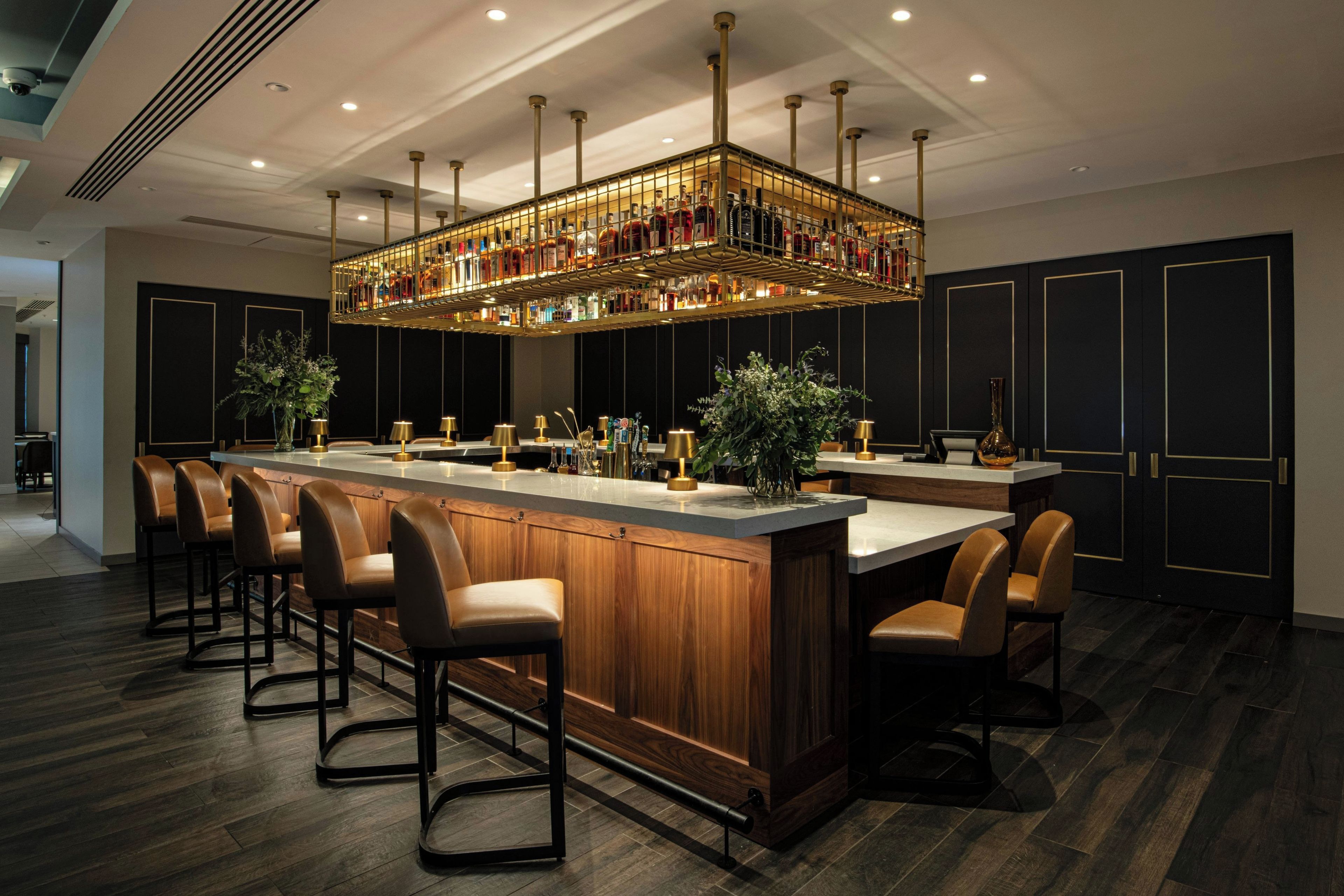 A bar area with a long counter, multiple stools, and a ceiling-mounted liquor display.