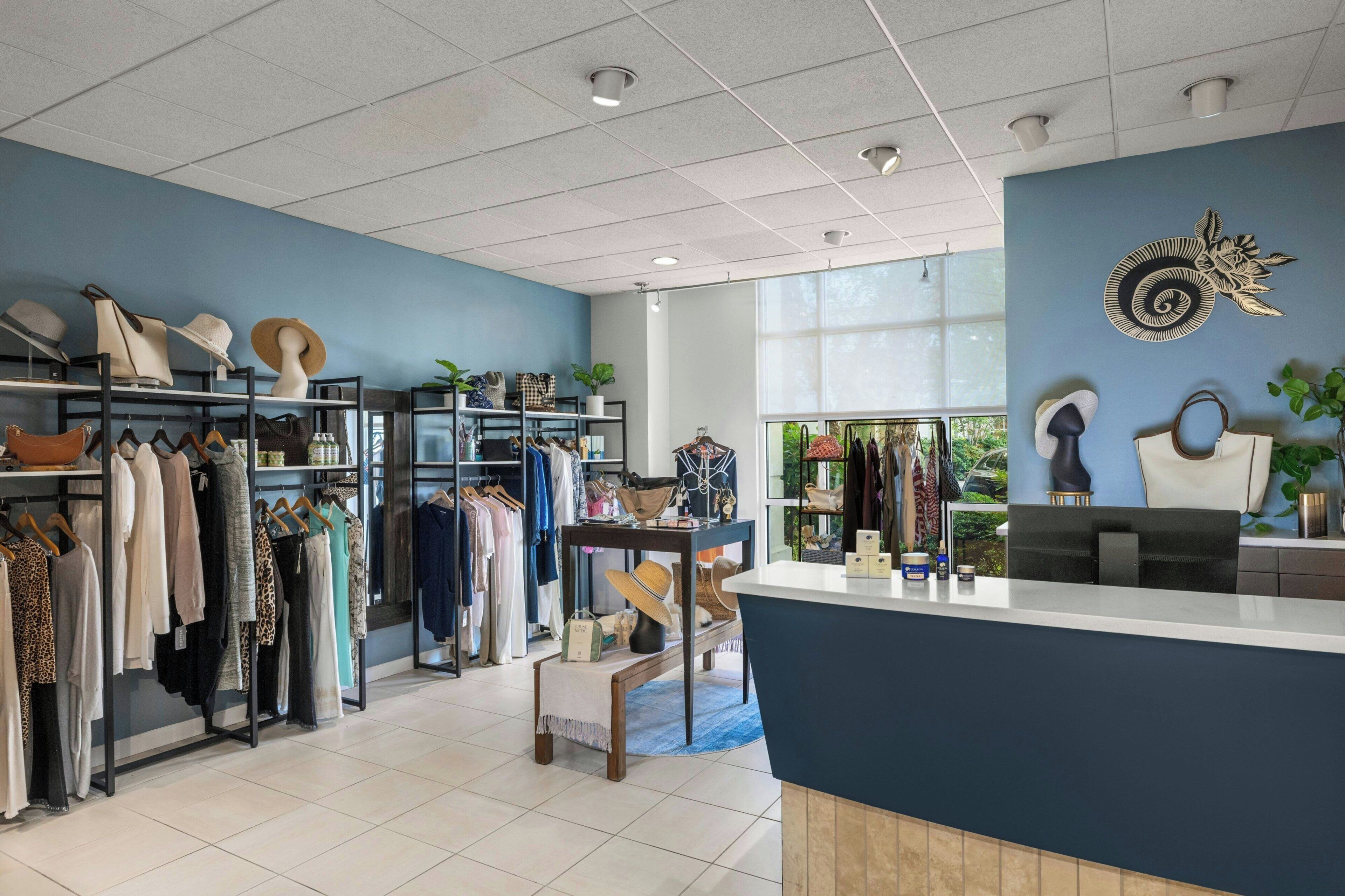 A retail store with clothing racks, a reception desk, and a large window with a view of greenery.