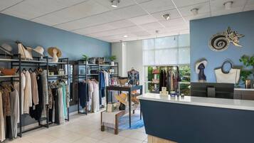 A retail store with clothing racks, a reception desk, and a large window with a view of greenery.