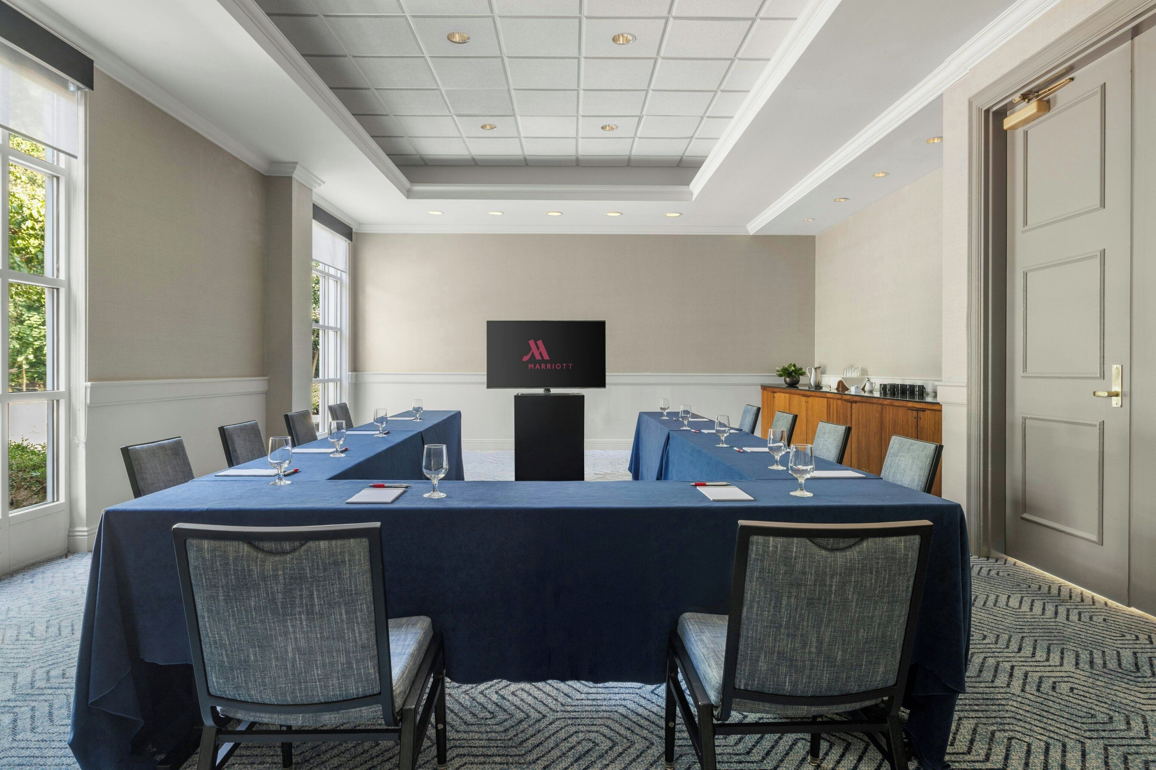 A conference room with a long table, chairs, and a television screen displaying the Marriott logo.
