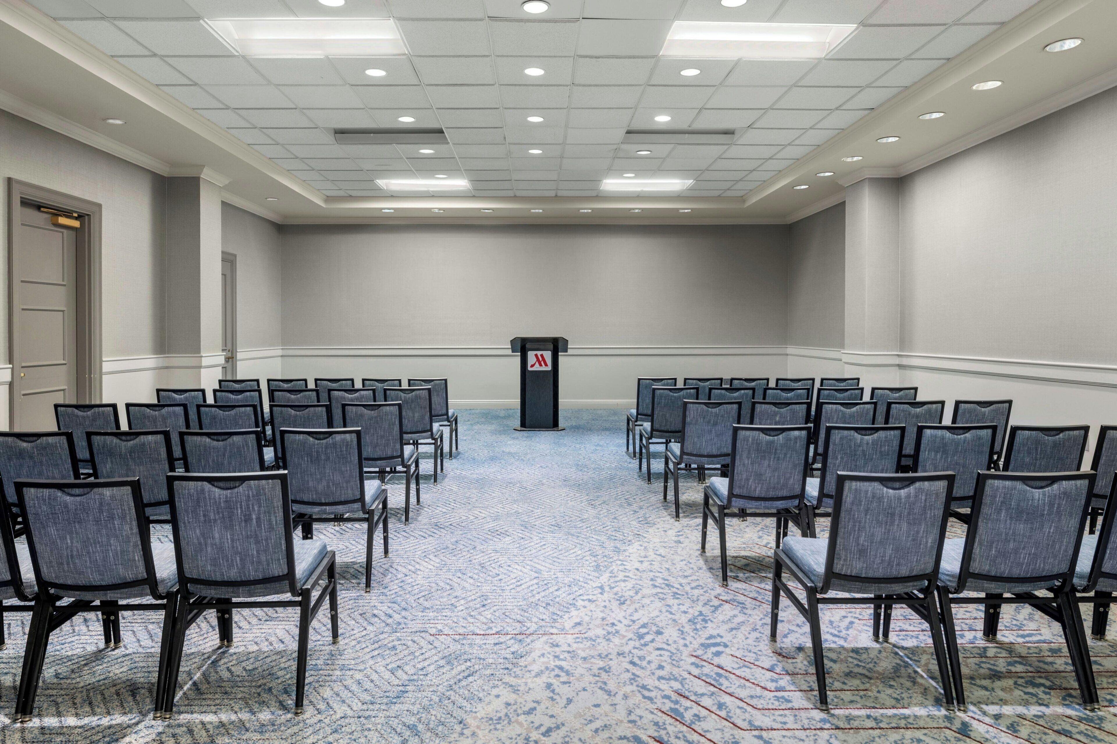 A conference room with rows of chairs, a podium, and a carpeted floor.