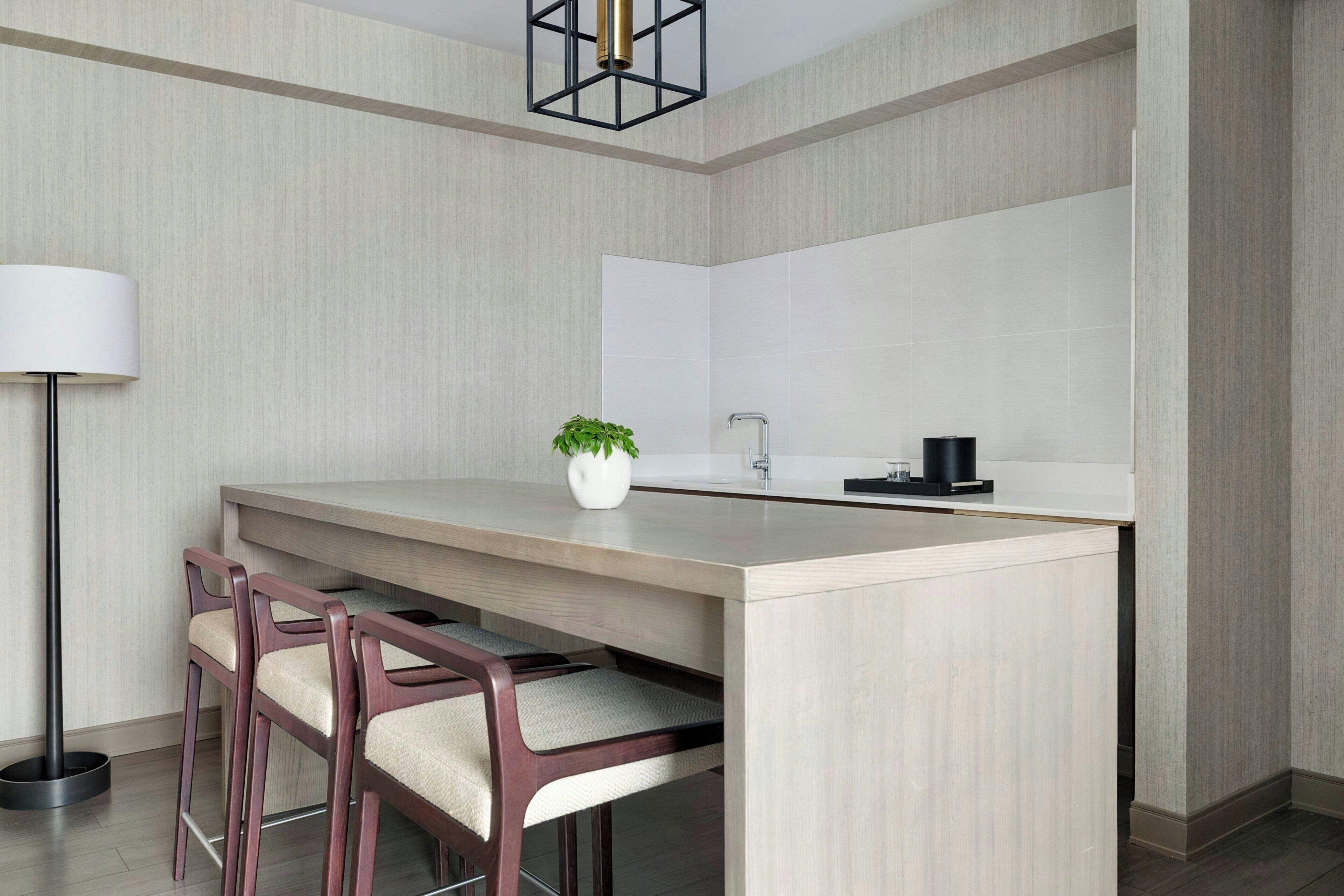 A modern kitchen with a central island, bar stools, a floor lamp, and a potted plant.