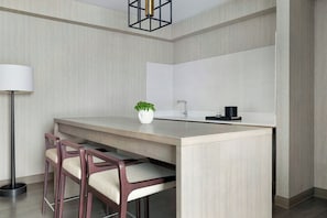 A modern kitchen with a central island, bar stools, a floor lamp, and a potted plant. - Mystic Marriott Hotel and Spa (Groton)