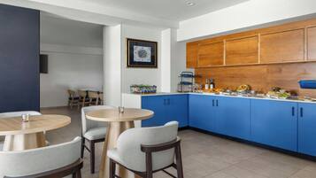 A modern kitchen with blue cabinets, a dining area with round tables and chairs, and a framed compass on the wall.