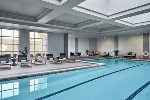 Una piscina interior con sillas de descanso y mesas, ventanas amplias y un diseño moderno en el techo.