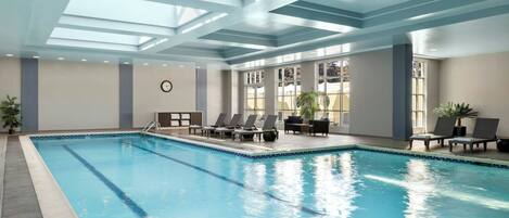 Uma grande piscina interior com pistas demarcadas, espreguiçadeiras e um relógio na parede.