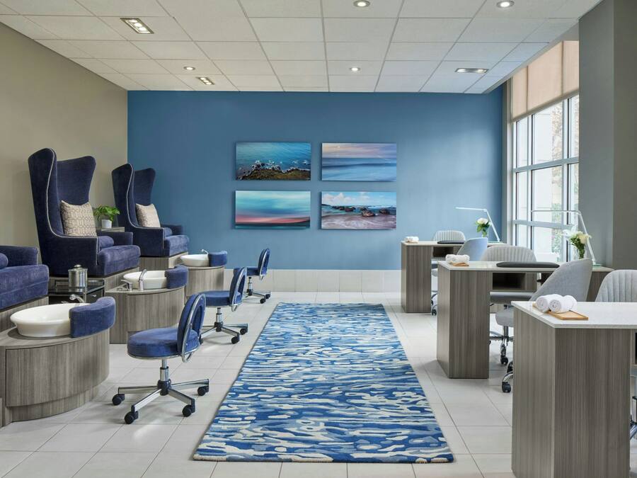 A modern spa room with a blue wall, four framed artworks, a blue patterned rug, and a reception desk with a computer and a plant.