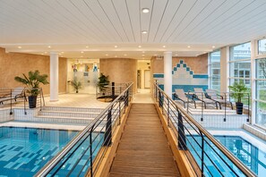 A hotel lobby with a pool area, featuring a wooden staircase, railings, and potted plants. - Seminaris Sunday See Hotel Potsdam (Potsdam)