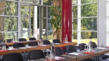 Ein Konferenzraum mit mehreren Tischen, Stühlen und einem großen Fenster mit Blick auf Bäume.