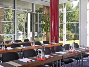 A conference room with multiple tables, chairs, and a large window with a view of trees. - Seminaris Sunday See Hotel Potsdam (Potsdam)