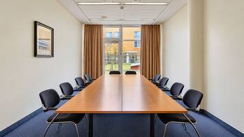 Ein Konferenzraum mit einem langen Tisch und Stühlen, großen Fenstern mit Vorhängen und einem gerahmten Bild an der Wand.