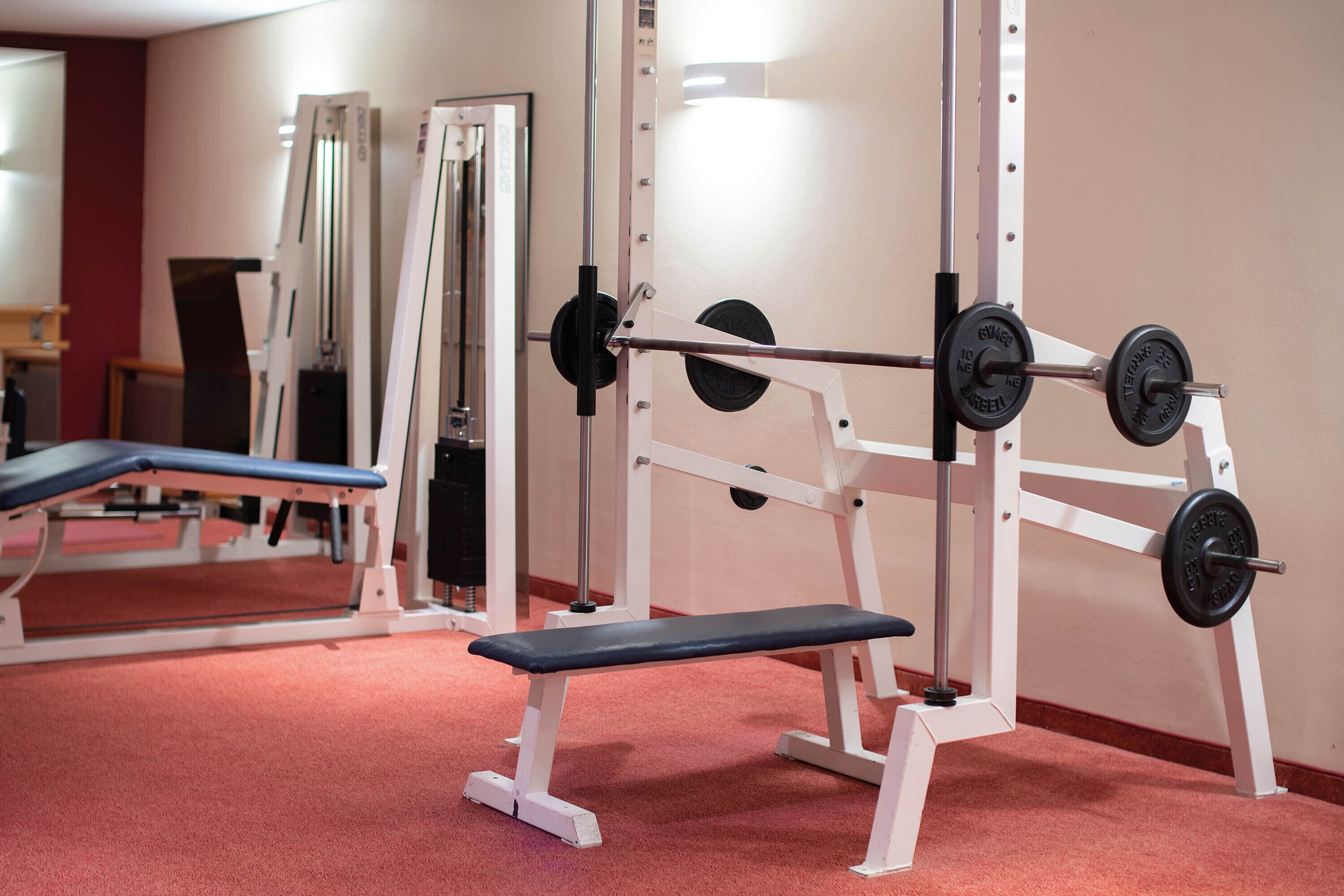 A gym with weightlifting equipment, benches, and mirrors.