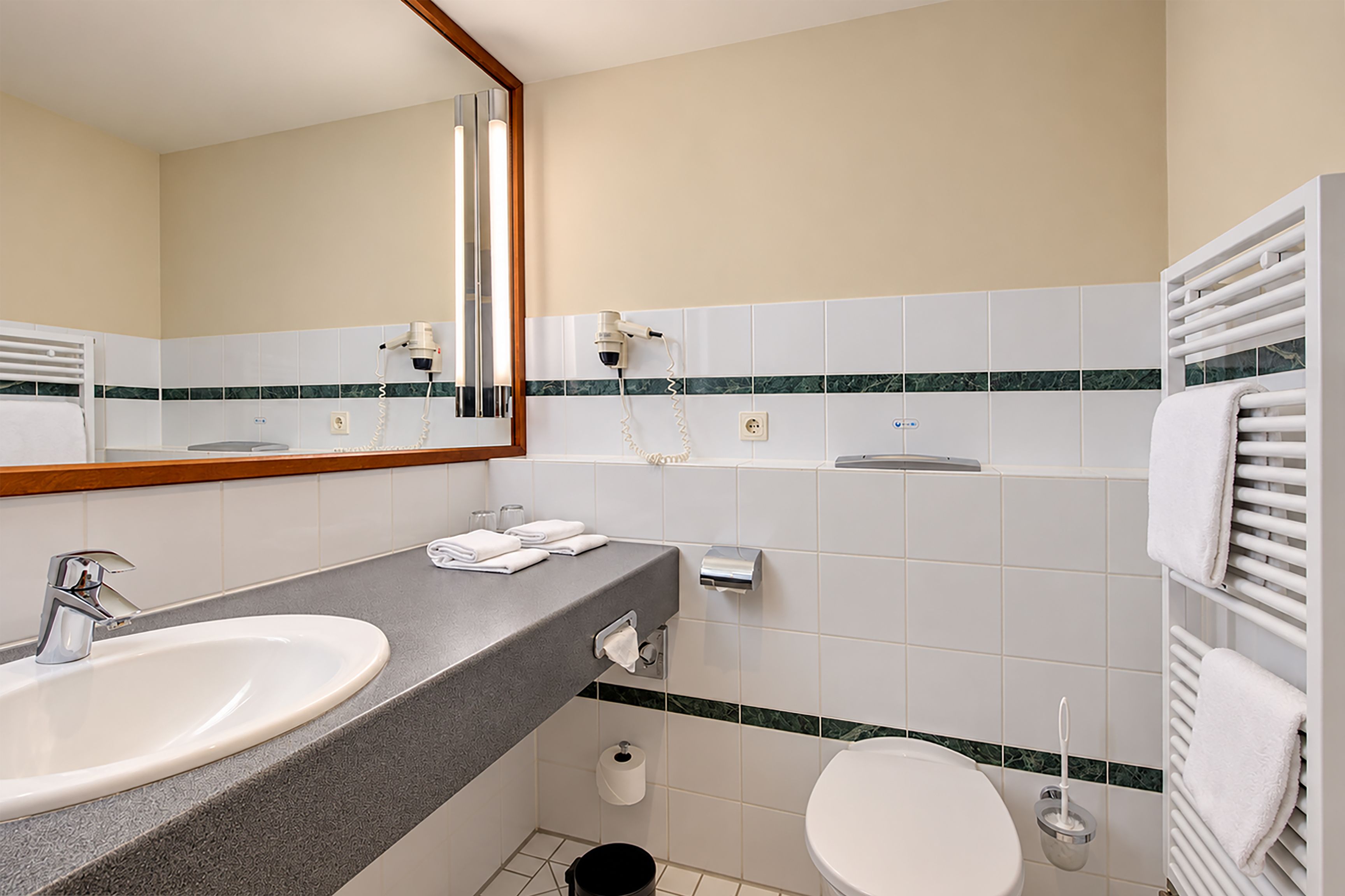 Un baño con lavamanos doble, inodoro, toallero y espejo.