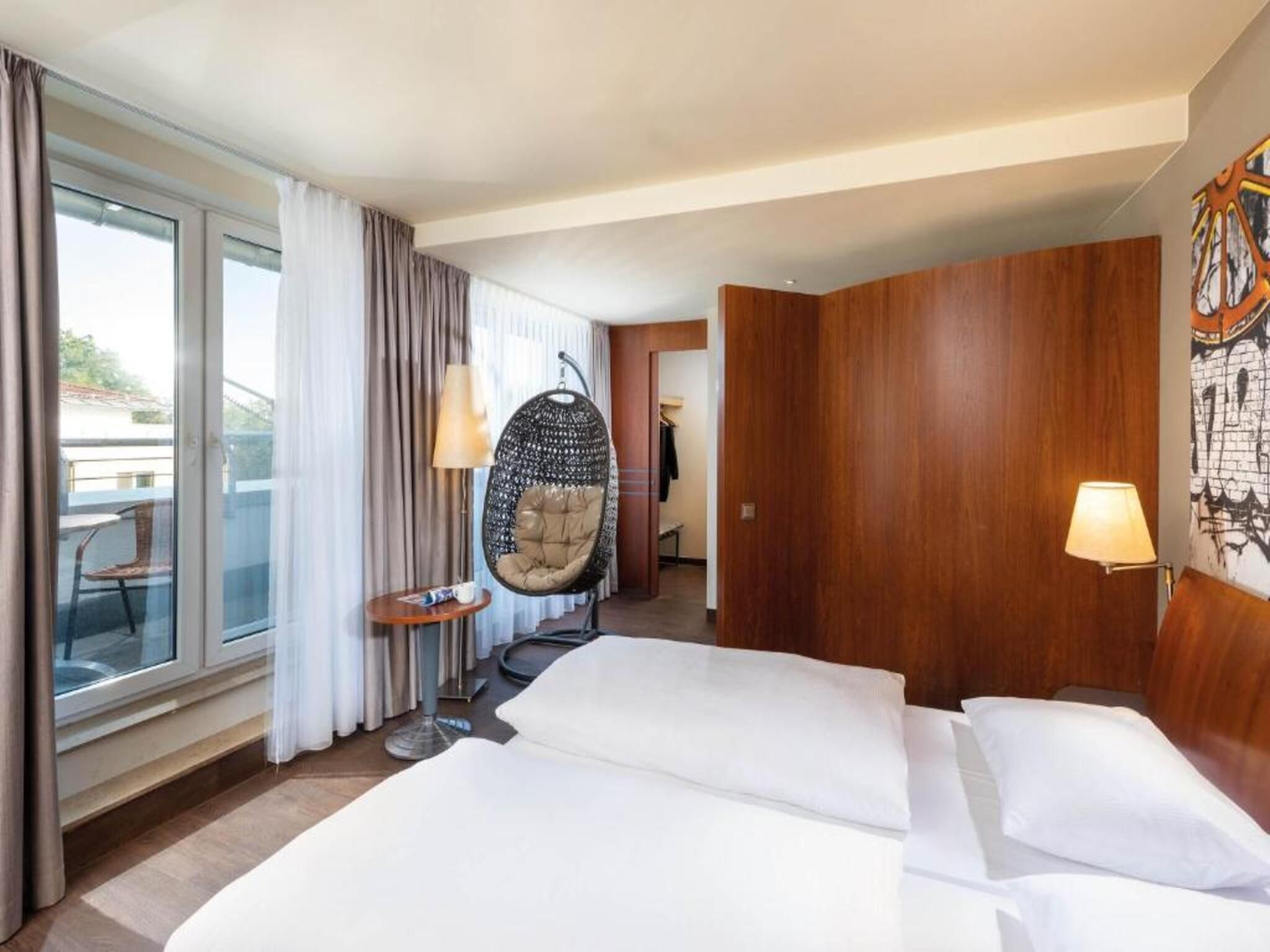 Habitación de hotel con una cama grande, una silla colgante, una mesita y vistas al exterior.
