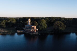 A historic building with a tower and arched windows, situated on a lake surrounded by trees. - Seminaris Sunday See Hotel Potsdam (Potsdam)