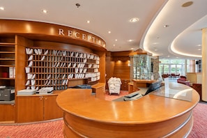 A reception area with a wooden reception desk, a large bookcase filled with books, and a glass display case. - Seminaris Sunday See Hotel Potsdam (Potsdam)