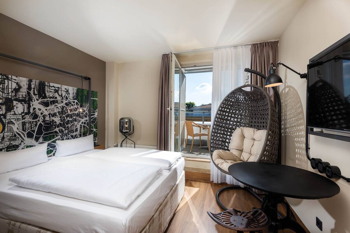 A hotel room with a bed, a desk, a chair, a TV, and a balcony with a view.