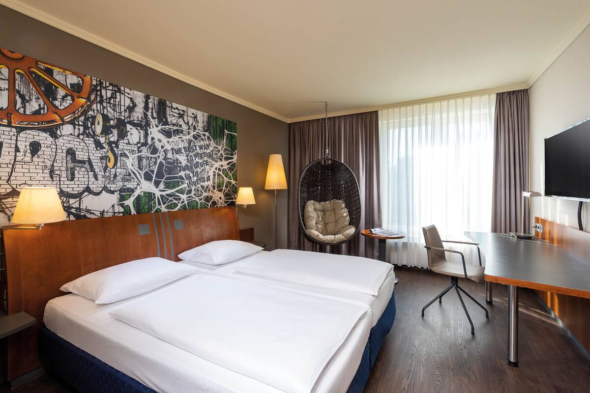 A hotel room with a large bed, two bedside tables, a desk, a chair, a television, and a wall mural.