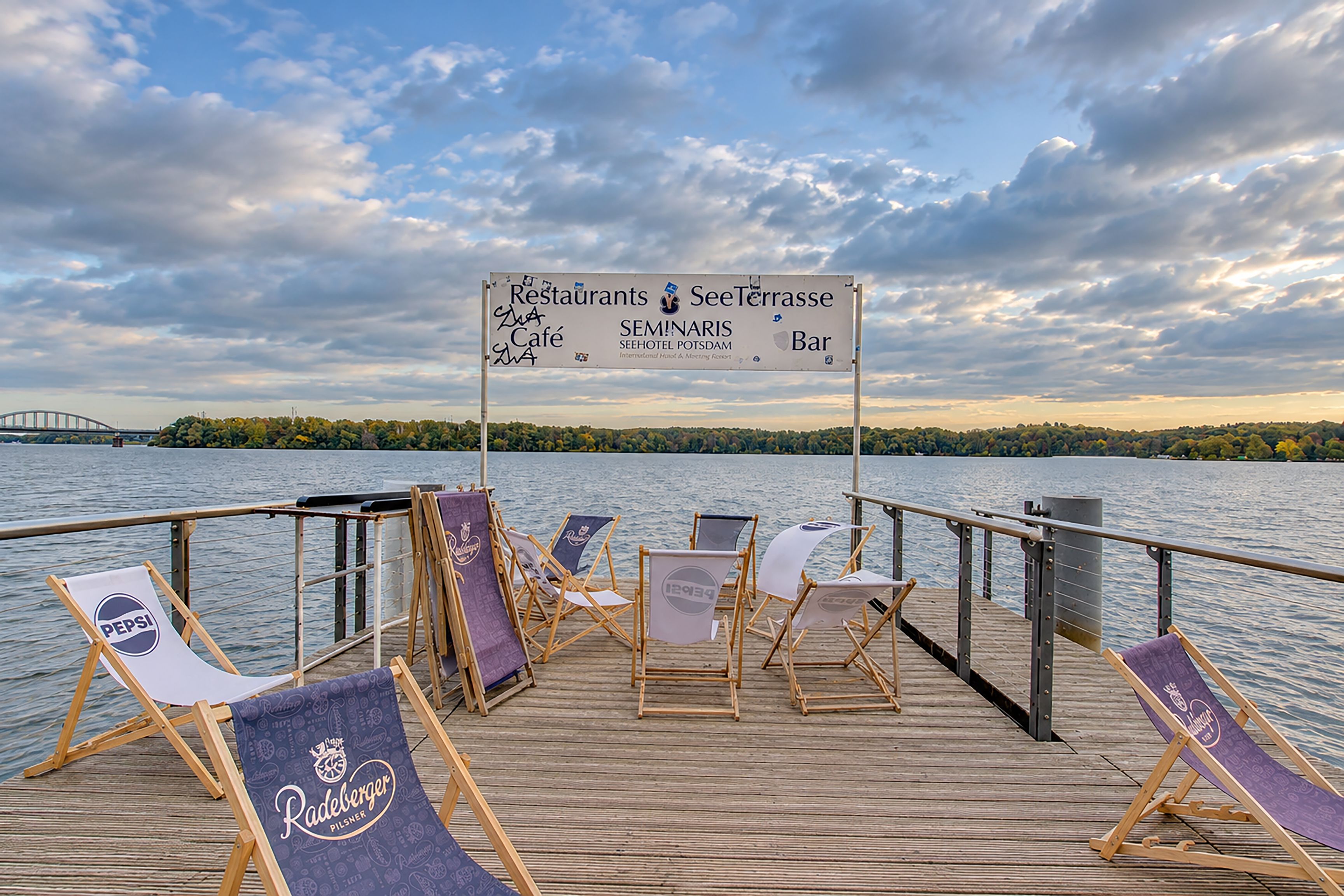 A wooden deck with lounge chairs and a signboard listing amenities like restaurants, a terrace, café, and bar.