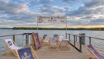 A wooden deck with lounge chairs and a signboard listing amenities like restaurants, a terrace, café, and bar.