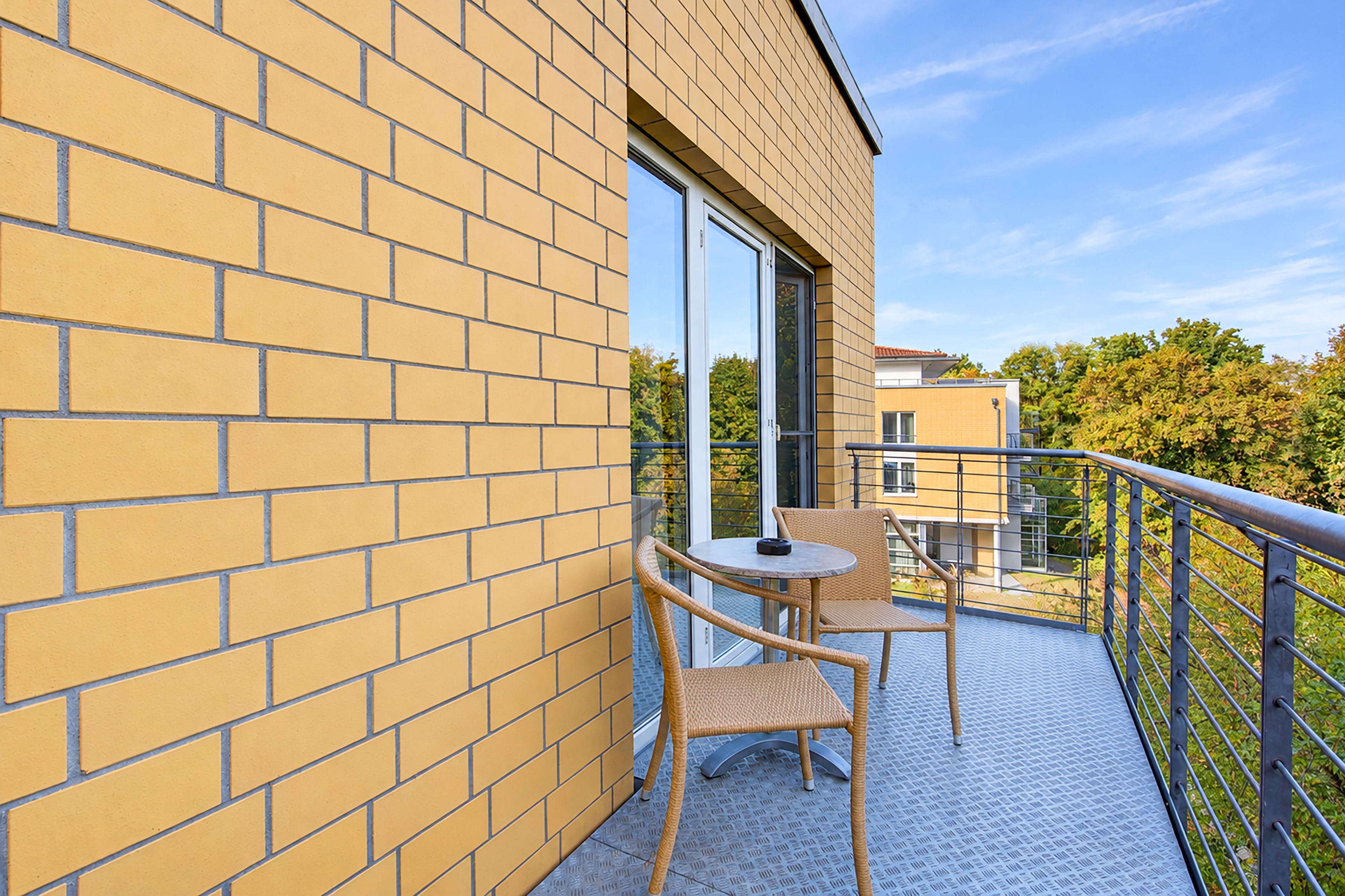 A balcony with a brick wall, a glass door, and two wicker chairs.