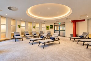 A room with multiple lounge chairs arranged in a semi-circle, a circular light fixture on the ceiling, and a door with an exit sign. - Seminaris Sunday See Hotel Potsdam (Potsdam)