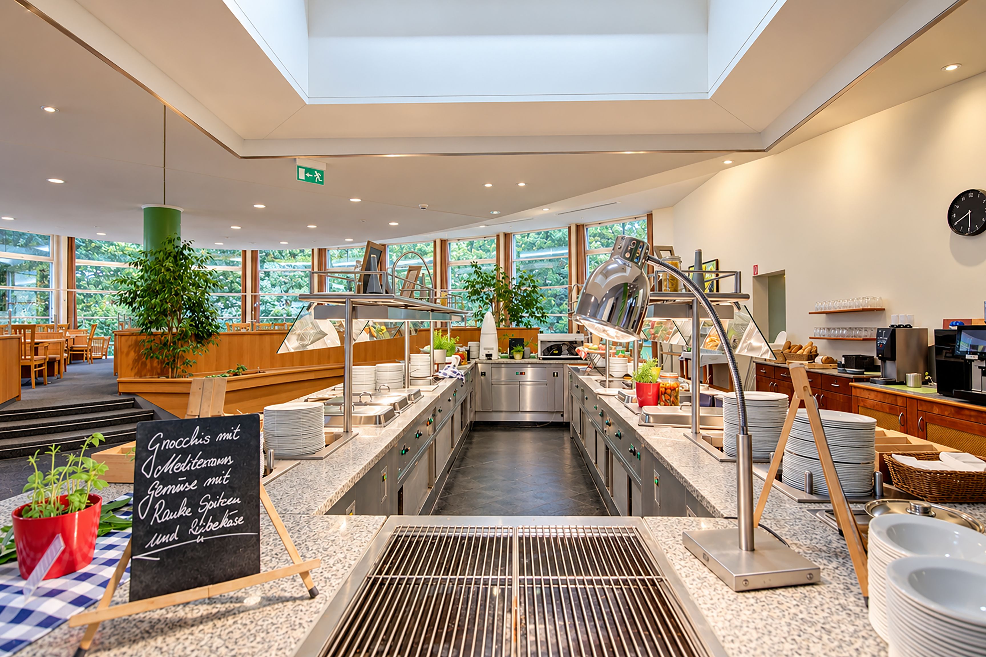 A modern kitchen with stainless steel appliances, a chalkboard menu, and large windows offering a view of greenery.
