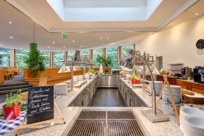 A modern kitchen with stainless steel appliances, a chalkboard menu, and large windows offering a view of greenery. - Seminaris Sunday See Hotel Potsdam (Potsdam)