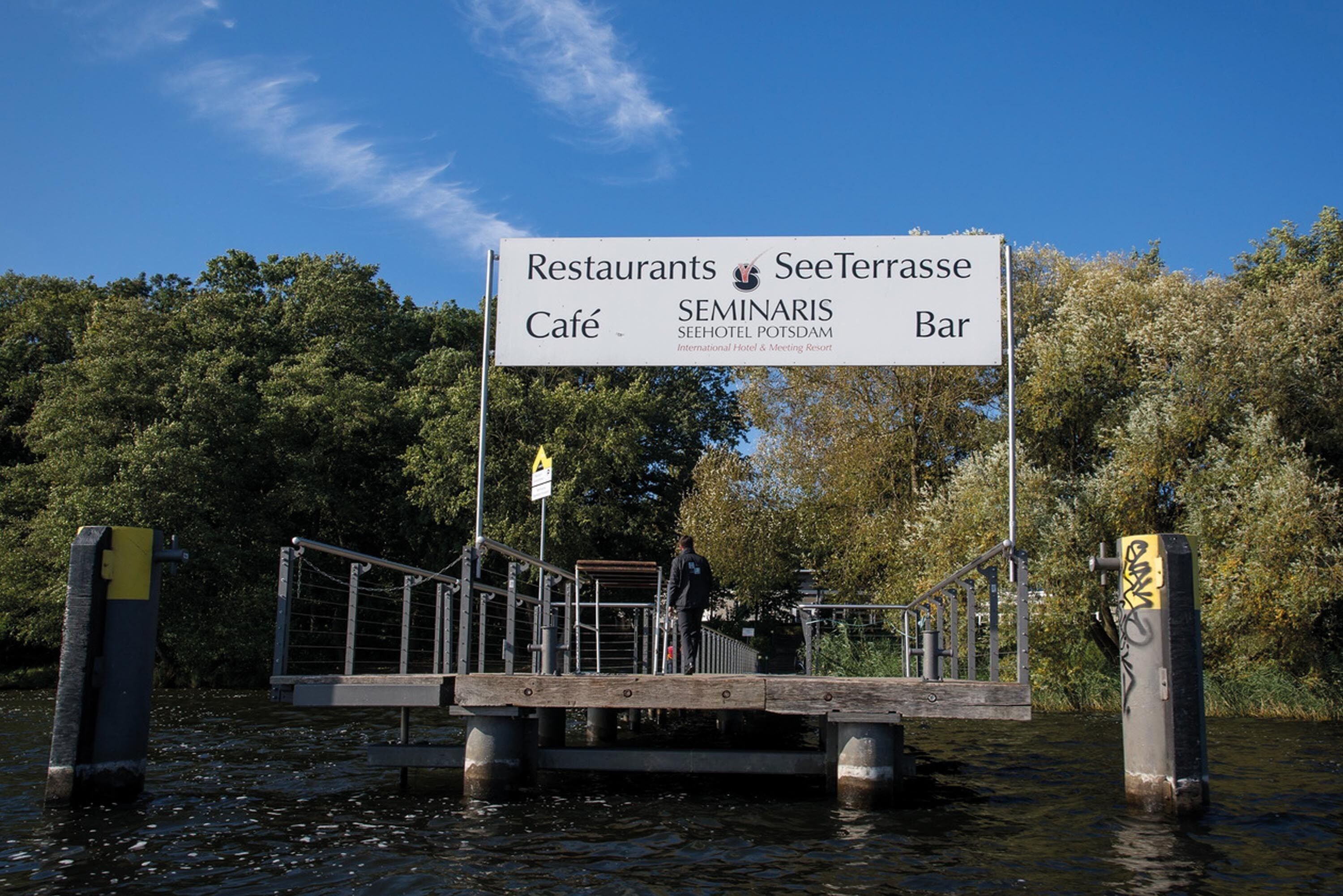 A signboard for a café and bar on a wooden platform over water, surrounded by trees.