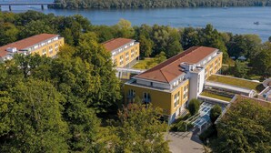 A yellow building with a red roof, surrounded by trees and a body of water with boats. - Seminaris Seehotel Potsdam (Potsdam)