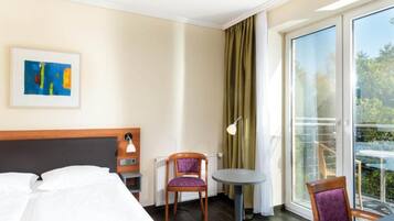 Una habitación de hotel con una cama, una silla, una mesita, una lámpara y un cuadro en la pared.