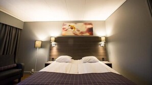 A hotel room with a large bed, two bedside tables, a headboard, a wall-mounted artwork, and a floor lamp.