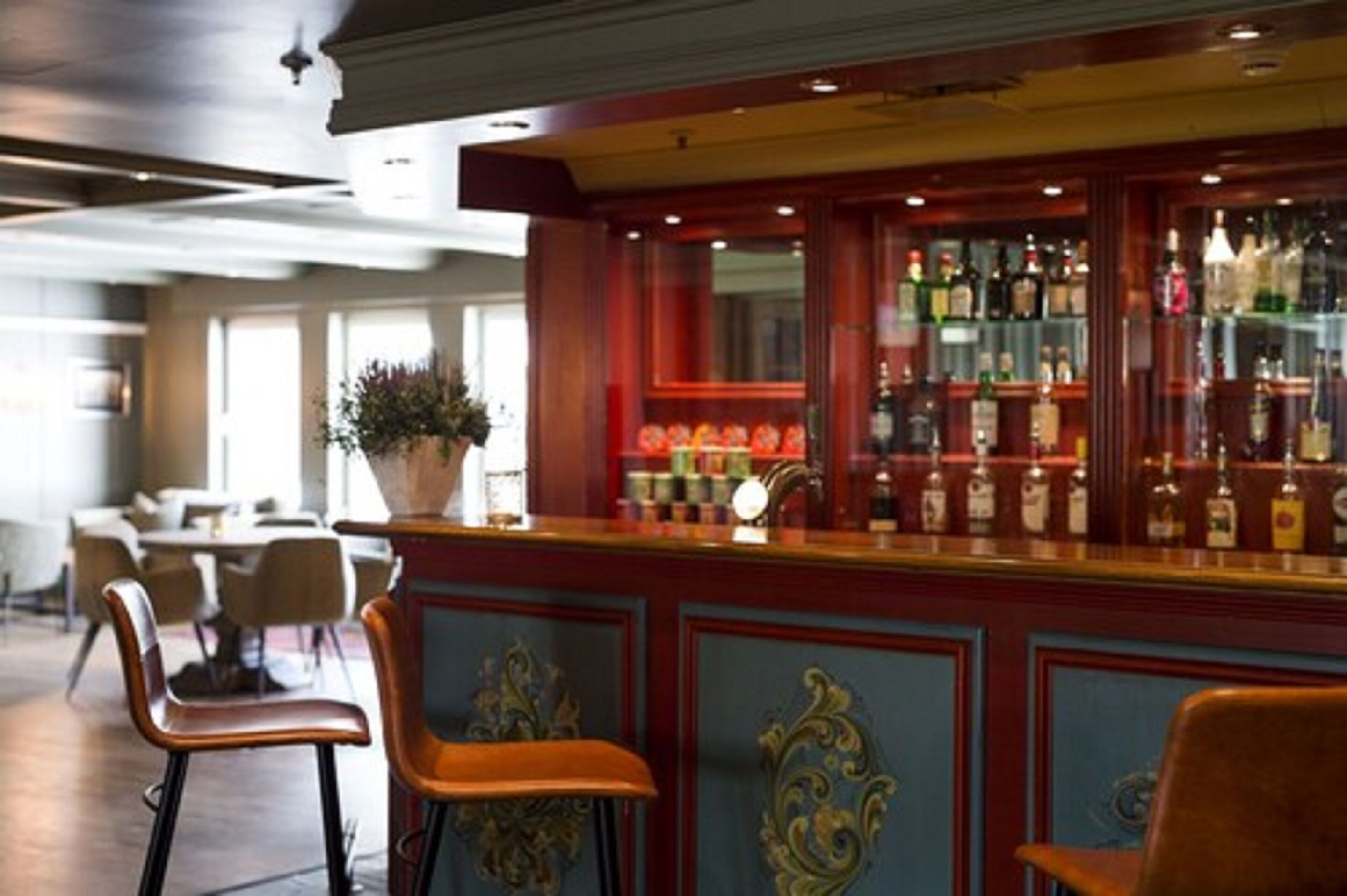 Zona de bar con mostrador de madera, taburetes y una variedad de botellas y vasos.
