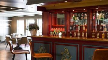 Zona de bar con mostrador de madera, taburetes y una variedad de botellas y vasos.