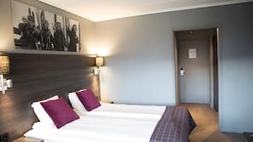 A hotel room with a large bed, two pillows, a headboard, a wall-mounted picture, two bedside lamps, and a carpeted floor.